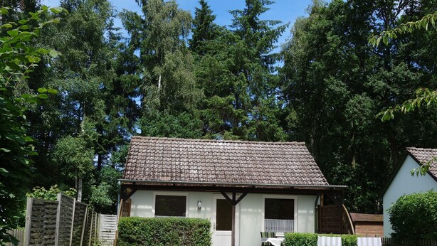 Une petite maison avec un toit en tuiles, un chemin pavé et deux chaises longues blanches dans la cour.