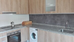 Une cuisine moderne avec des meubles en bois, un four encastré, un lave-linge, une machine à café et un évier.