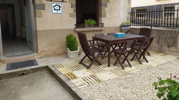Une cour avec une table et des chaises en bois, un pot de fleurs et un panneau indiquant qu’il s’agit d’un bien immobilier à louer.
