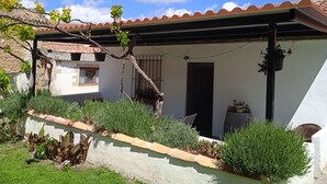 Un patio couvert avec un mur blanc, un toit en tuiles et des plantes en pot.