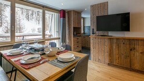 A modern kitchen with wooden cabinetry, a dining area with a table set for four, and a large TV mounted on the wall. - Elegant apartment - 6 guests near slopes (Val-d'Isère)