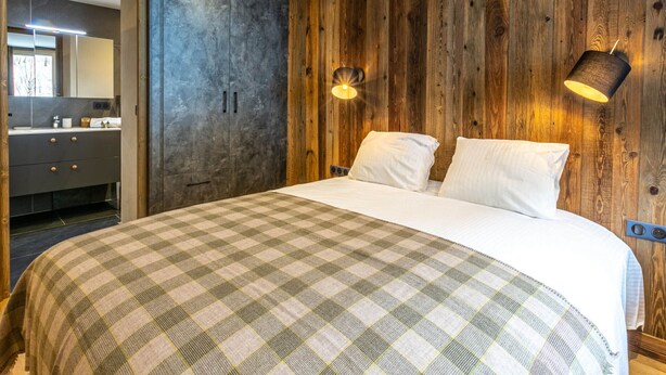 A bedroom with a wooden wall, a bed with a checkered blanket, a nightstand, and a wall-mounted lamp. - Elegant apartment - 6 guests near slopes (Val-d'Isère)