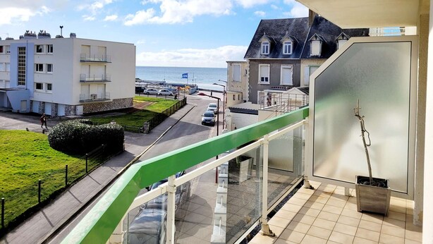 Un balcon donnant sur une zone côtière, avec vue sur une route, des voitures garées et des bâtiments.