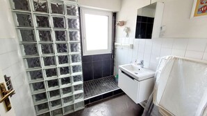 Une salle de bain avec une douche, un lavabo et une fenêtre.