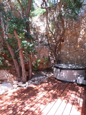 Relax in the hot tub surrounded by lush greenery and a natural stone wall.
