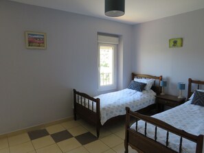 Two comfortable beds with matching nightstands, a large window, and checkered tile floor.