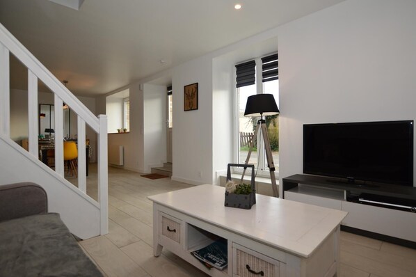 Una sala de estar moderna con un televisor de pantalla plana, una mesa de centro blanca y una escalera que lleva a otra habitación.