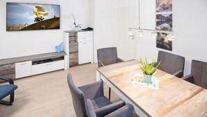 Uma área de refeições moderna com mesa de madeira, cadeiras estofadas em cinza, um banco e uma planta em vaso.