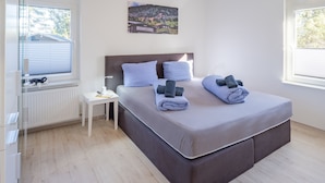 Quarto com cama, mesa de cabeceira, abajur e janela com persianas.