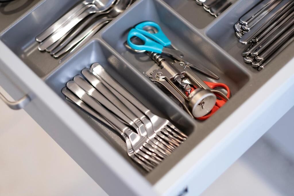 A drawer containing various kitchen utensils including forks, knives, and scissors.