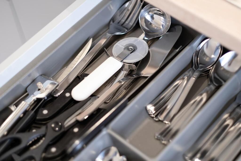 A drawer containing various utensils including knives, spoons, and a can opener.