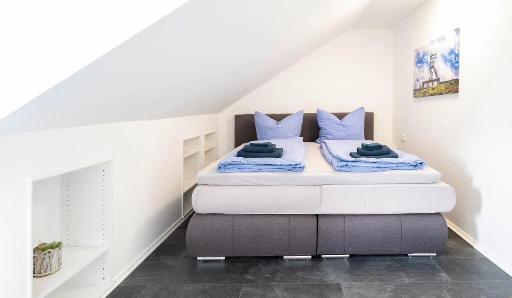 Un dormitorio moderno y compacto con cama tipo loft, estanterías empotradas y una pequeña planta en maceta.