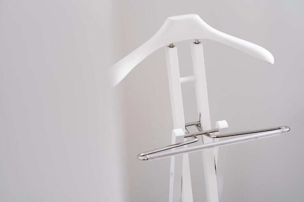 A white, modern, minimalist coat rack with a sleek, metallic handle.