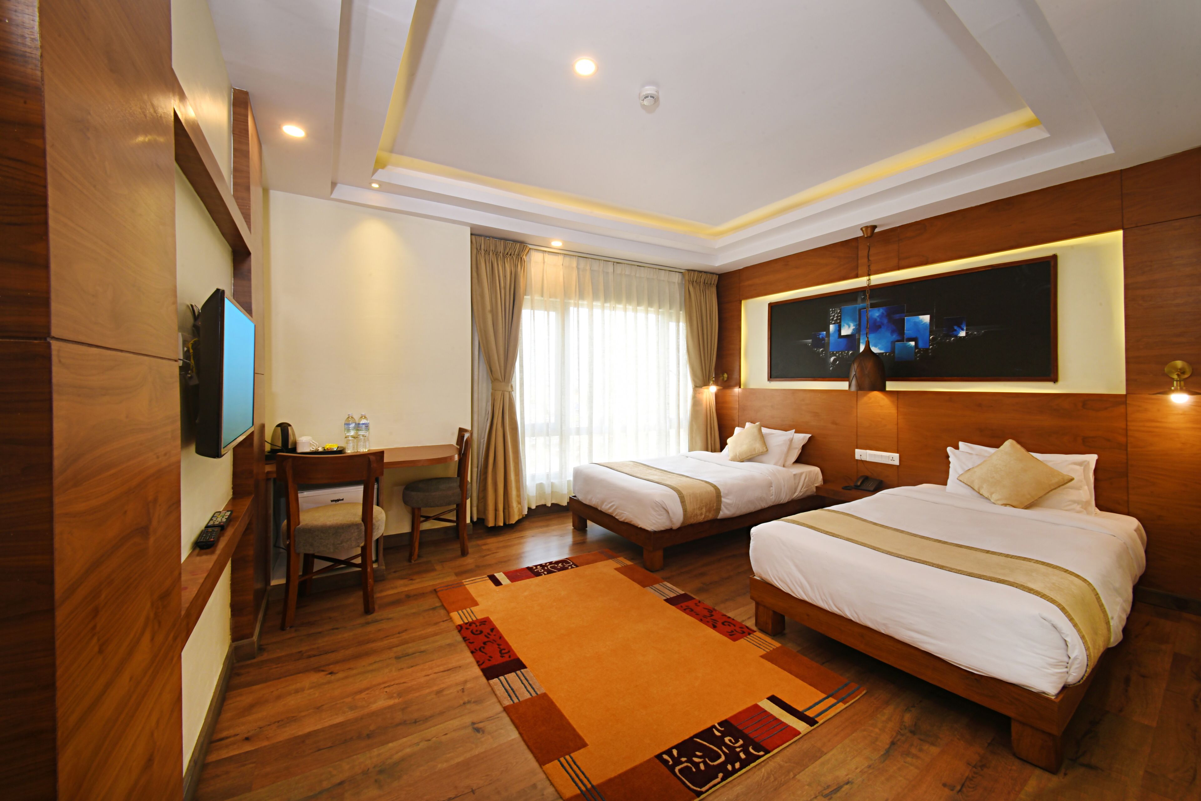 A hotel room with two beds, a desk with a chair, a television, and a large window with curtains.
