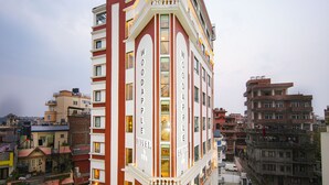 Un hotel de varios pisos con el letrero 'WOODAPPLE HOTEL', que presenta un estilo arquitectónico clásico y un balcón en el segundo piso.