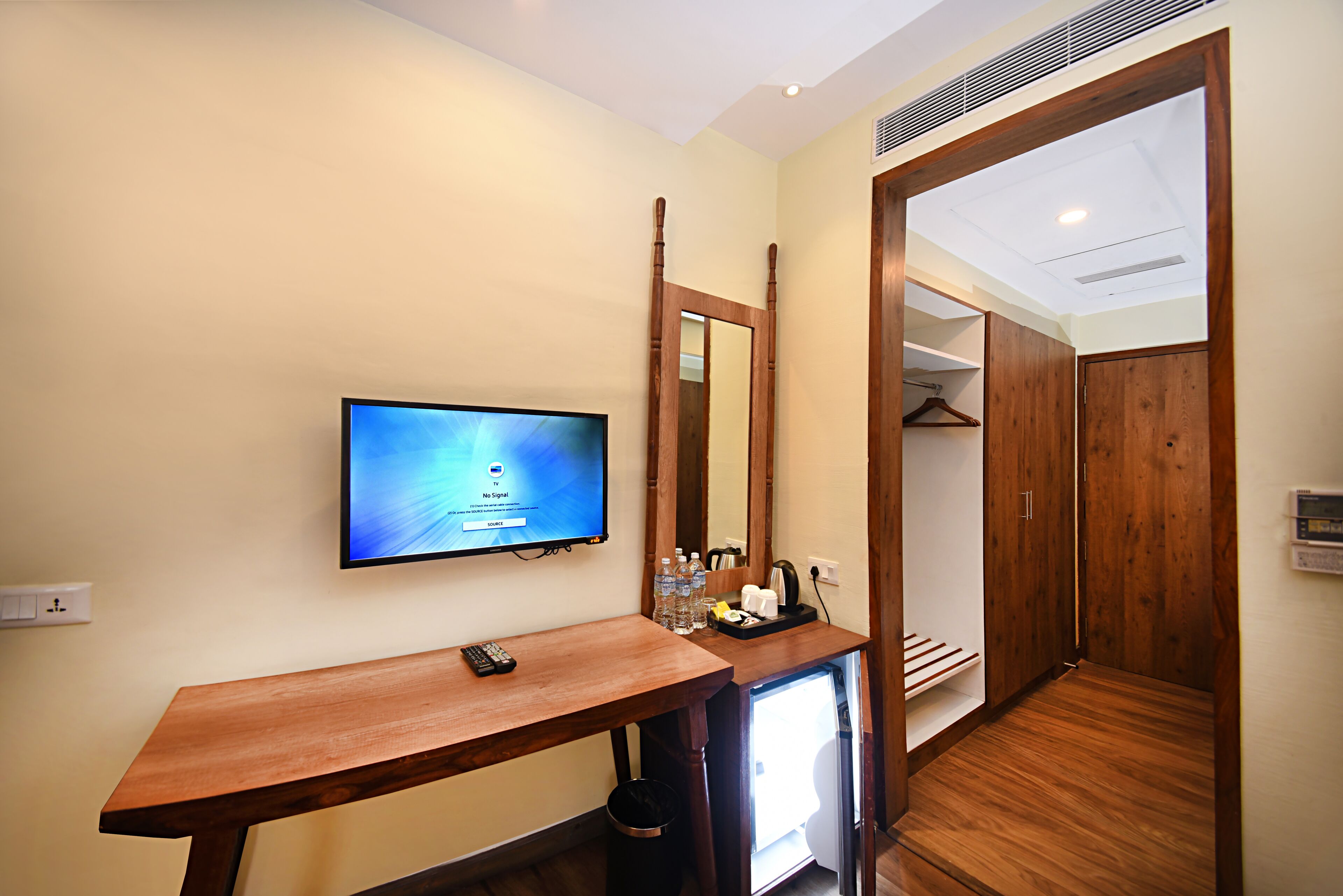 A hotel room with a wooden desk, a television, a mirror, and a walk-in closet.