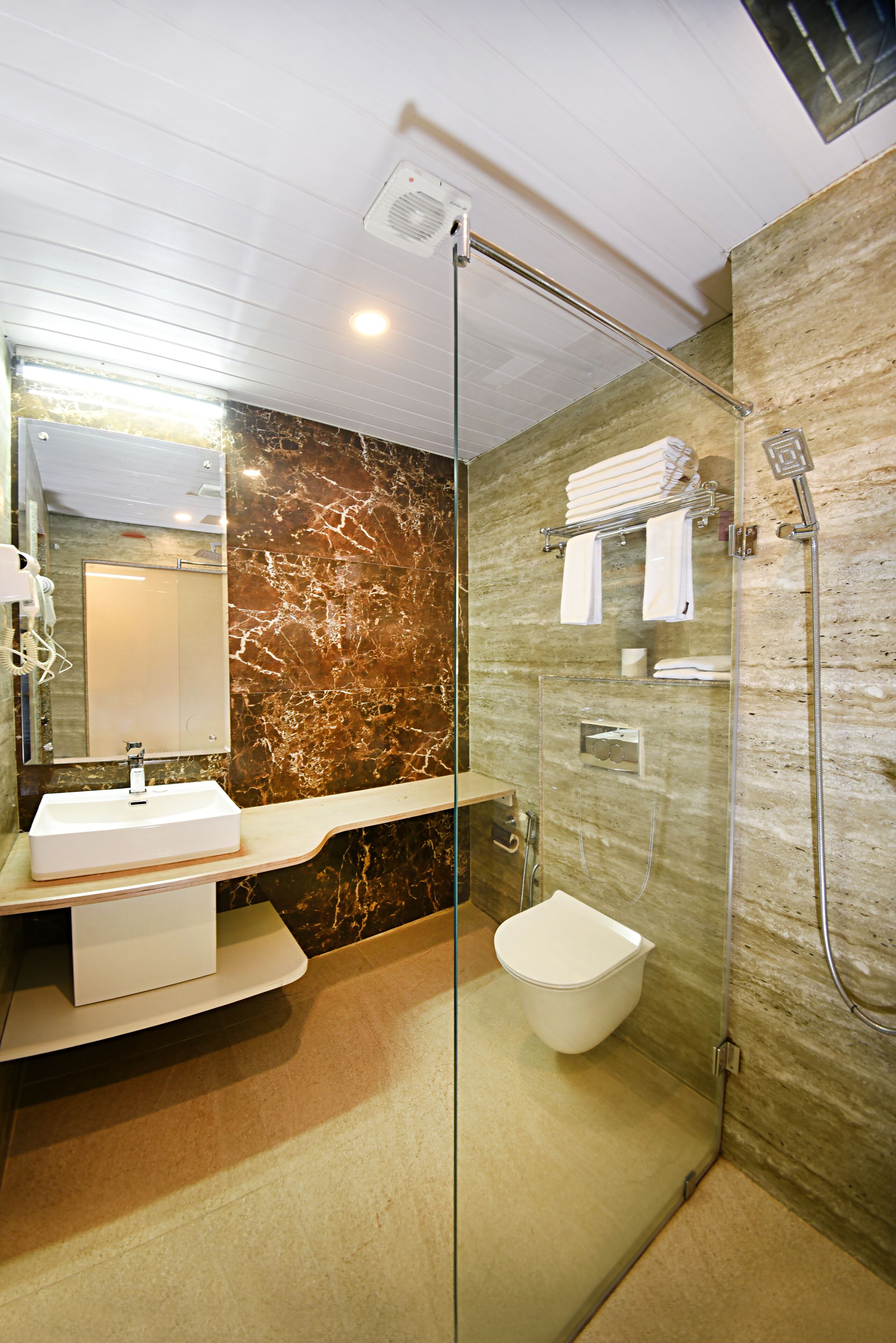A modern bathroom with a glass-enclosed shower, a white sink, and marble walls.