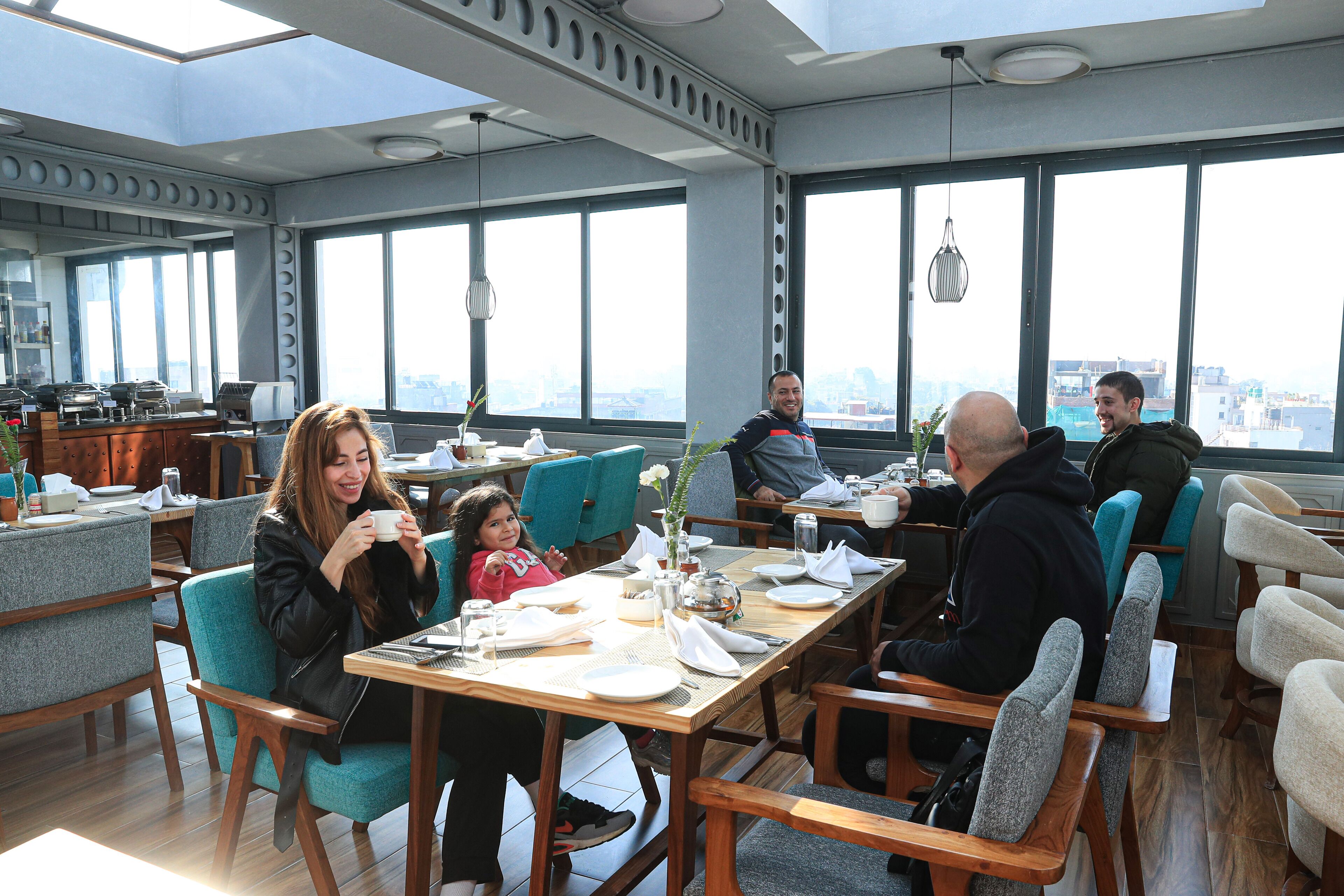 A modern dining area with high ceilings, large windows, and a city view.