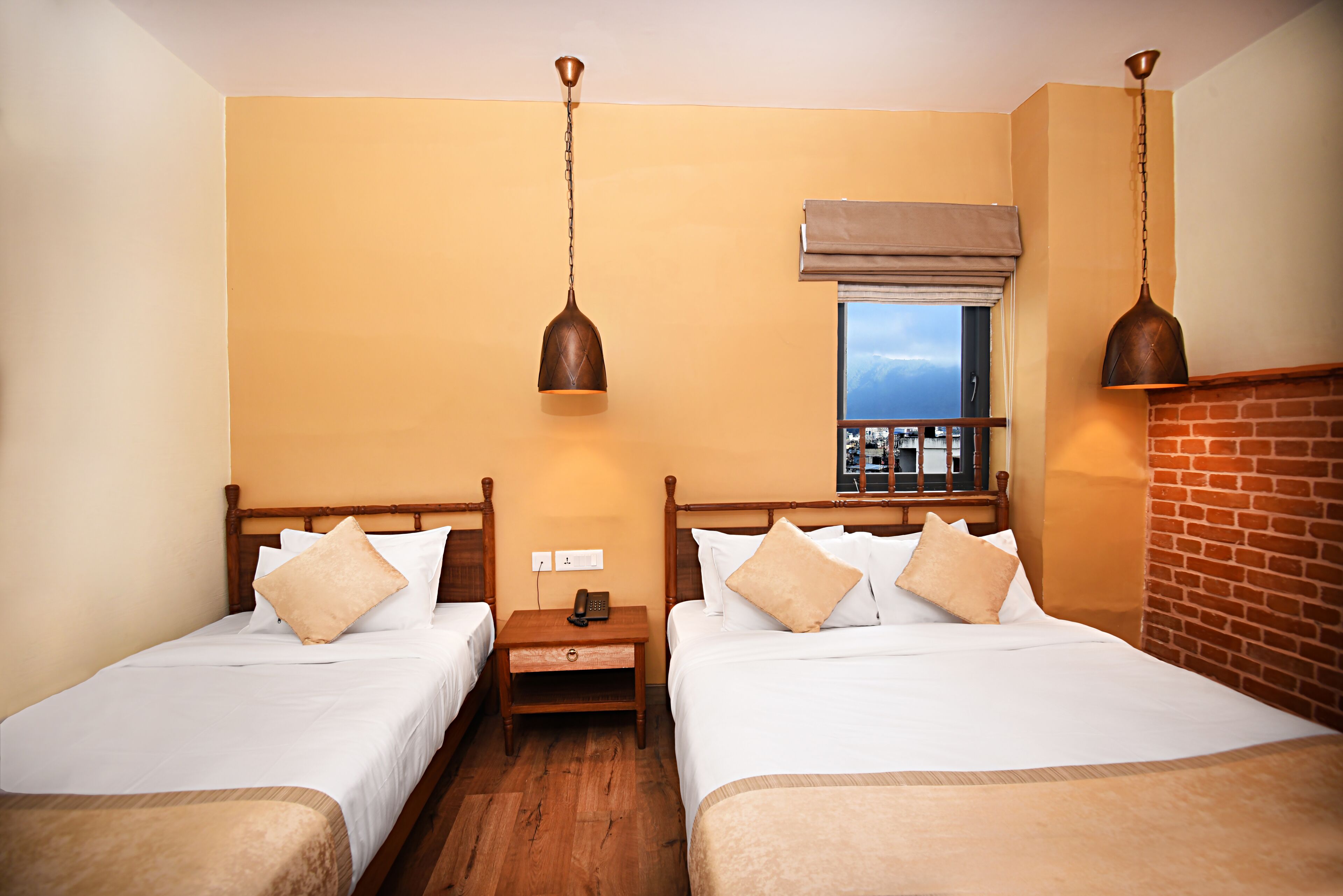 A hotel room with two single beds, wooden headboards, a nightstand with a phone, and a window with a view.