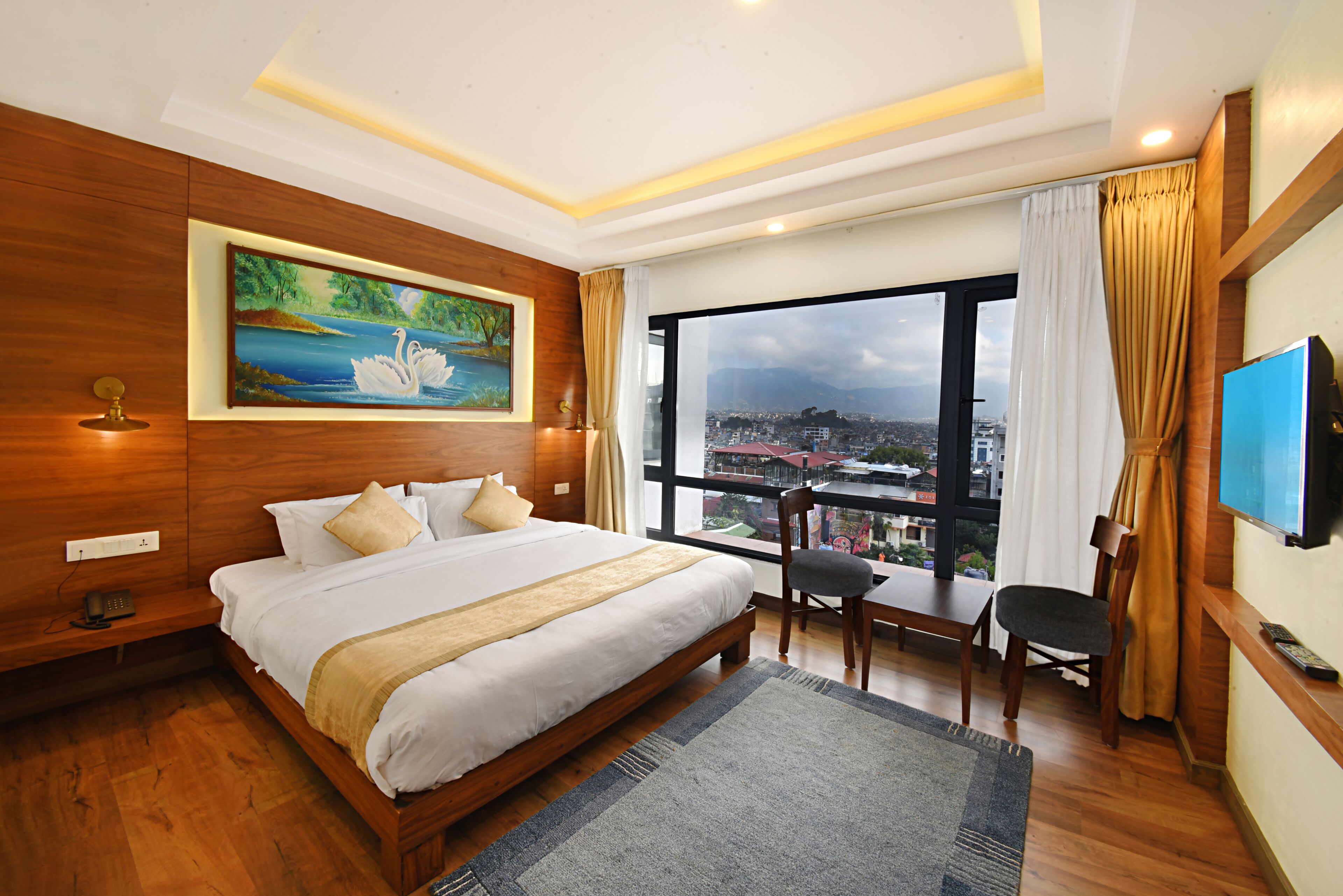 A hotel room with a large bed, a desk, a chair, a TV, and a painting of a swan on a lake.