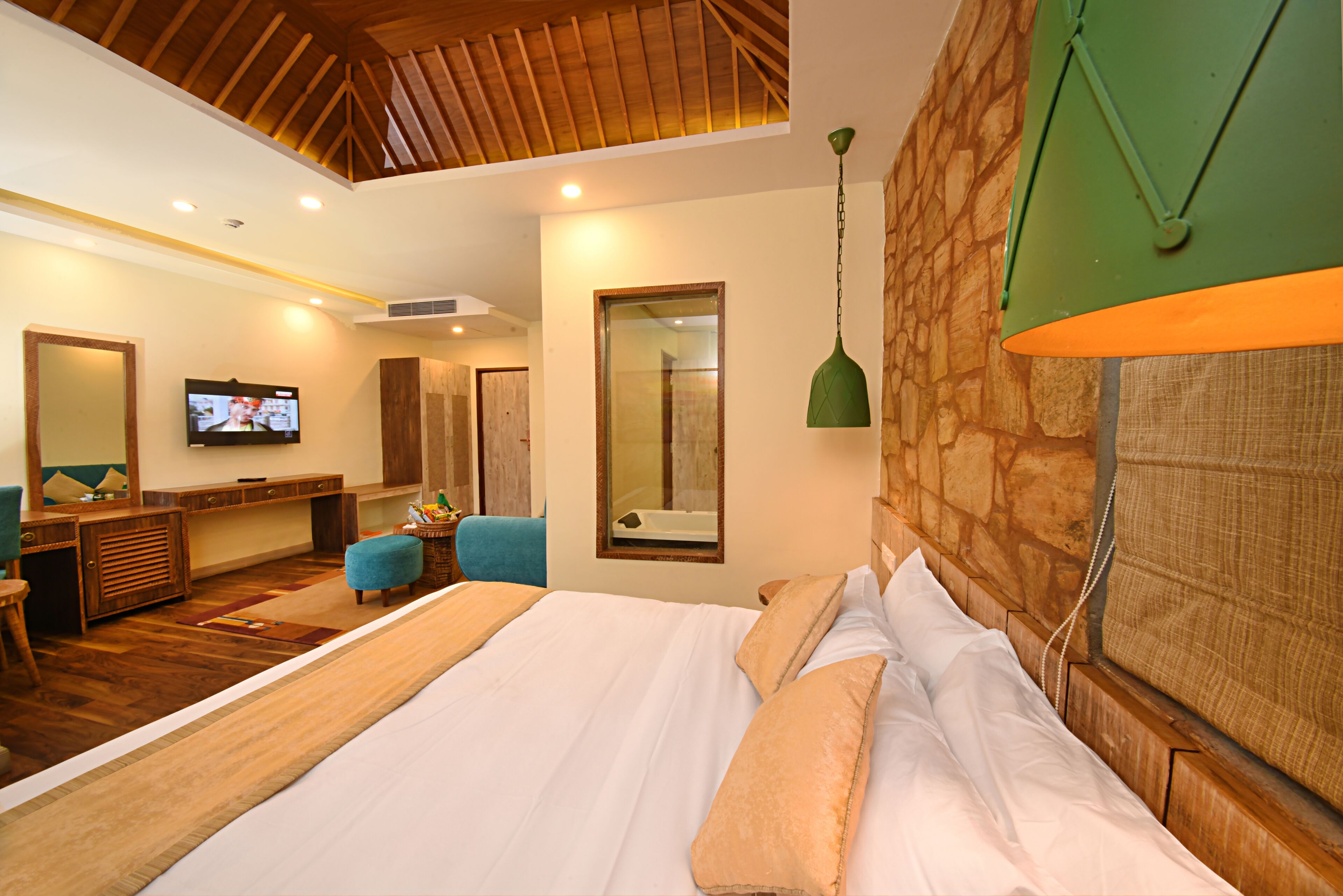 A bedroom with a large bed, a TV, a desk, and a stone wall.