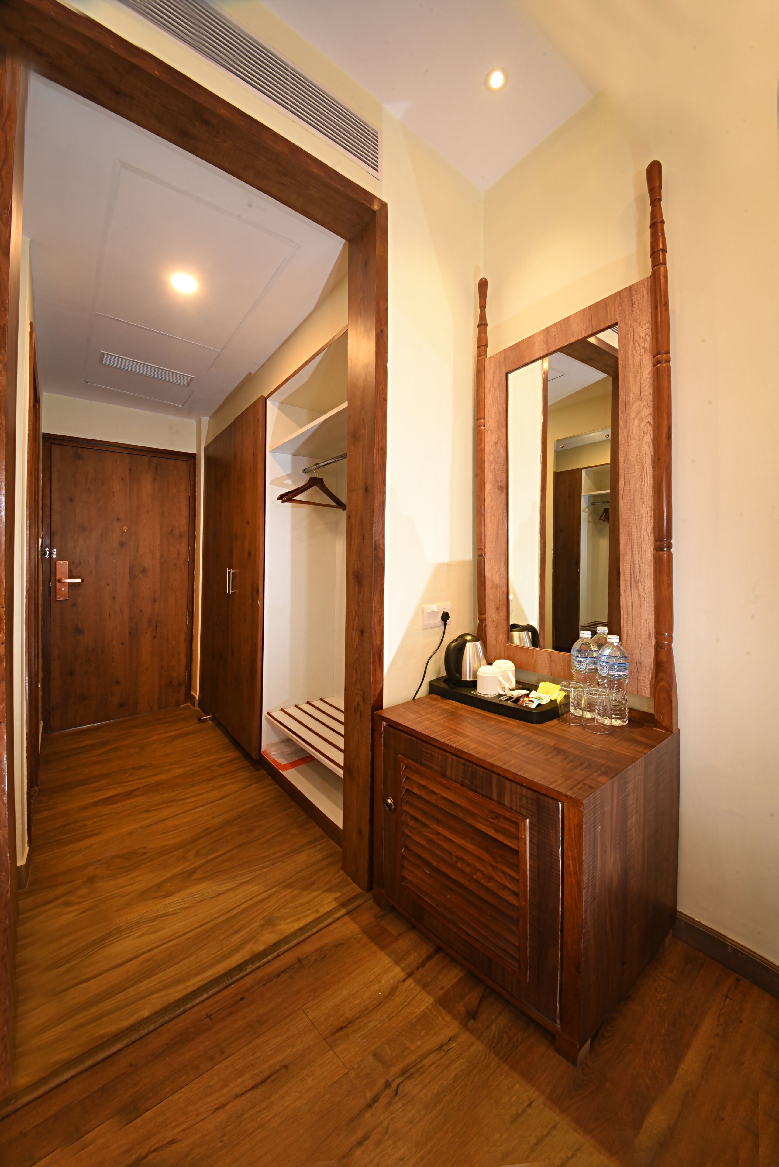 A hallway with wooden flooring, a wooden wardrobe, a mirror, and a tray with toiletries.