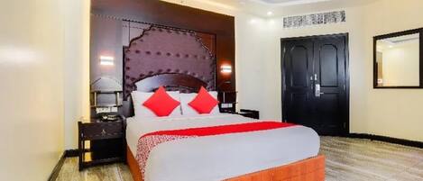 A hotel room with a large bed, a wooden headboard, a nightstand, and a black door.