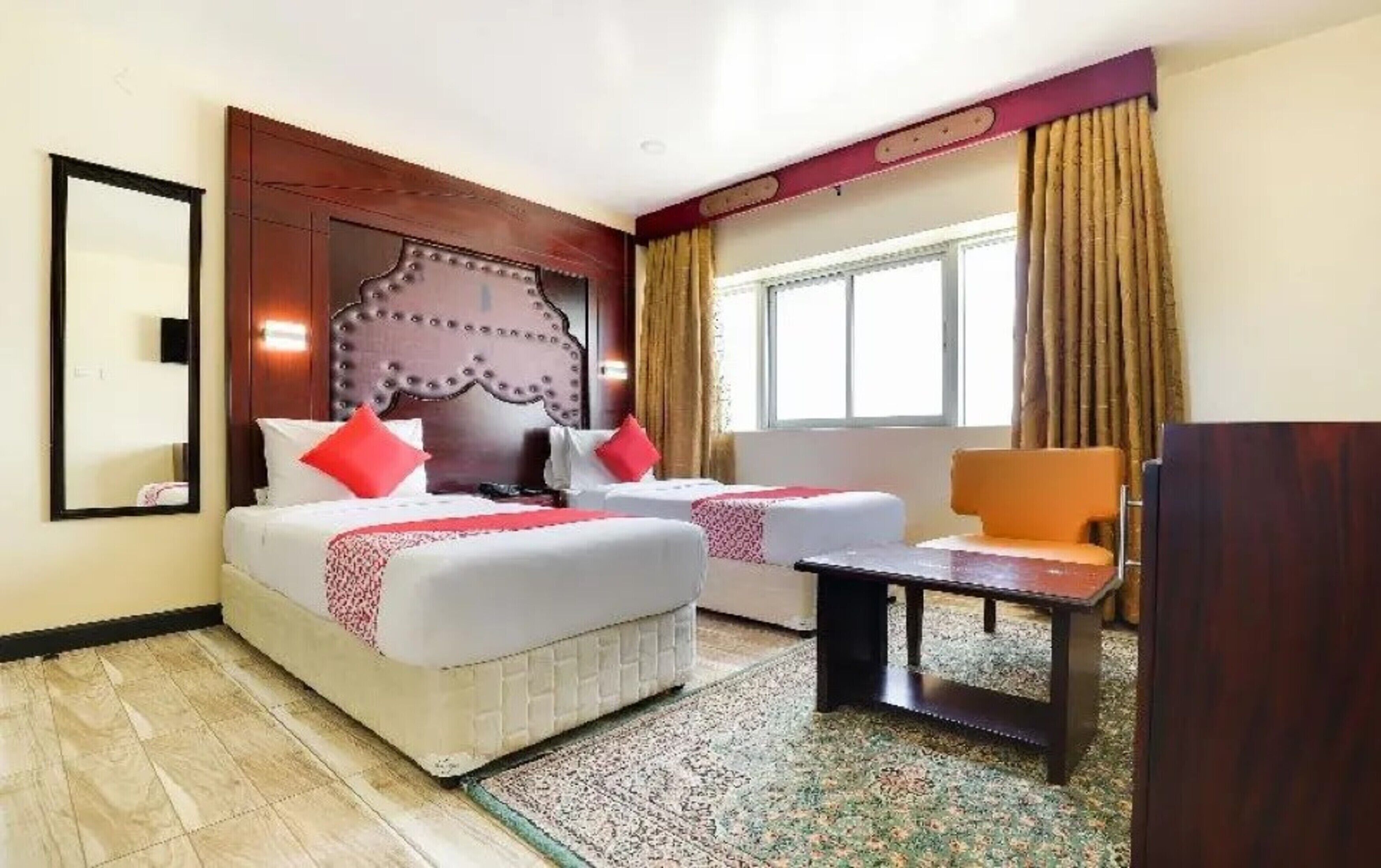 A hotel room with two beds, a wooden headboard, a small table, and a chair.