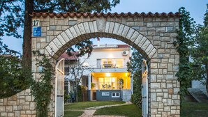 A stone archway leading to a building with a balcony, a number sign, and a clear pathway.