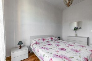 A bedroom with a bed, a nightstand, a dresser, a mirror, and a vase with flowers. - GuestHost - Viareggio Roomy House with Private Courtyard! x8 (Viareggio)