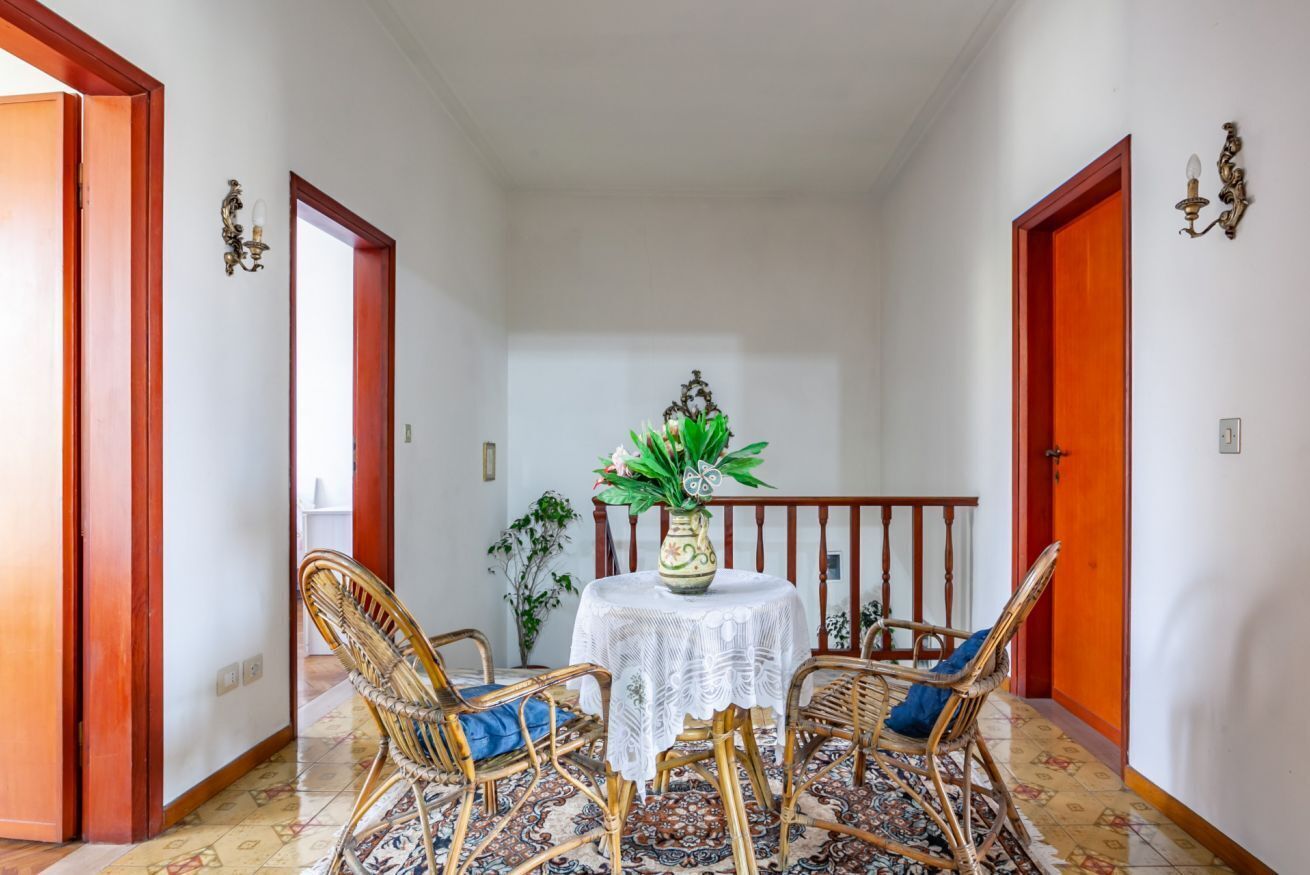 A hallway with a round table, wicker chairs, a patterned rug, and a potted plant.