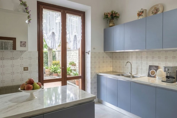 A kitchen with a marble countertop, a sink, cabinets, and a view through a door to a garden.
