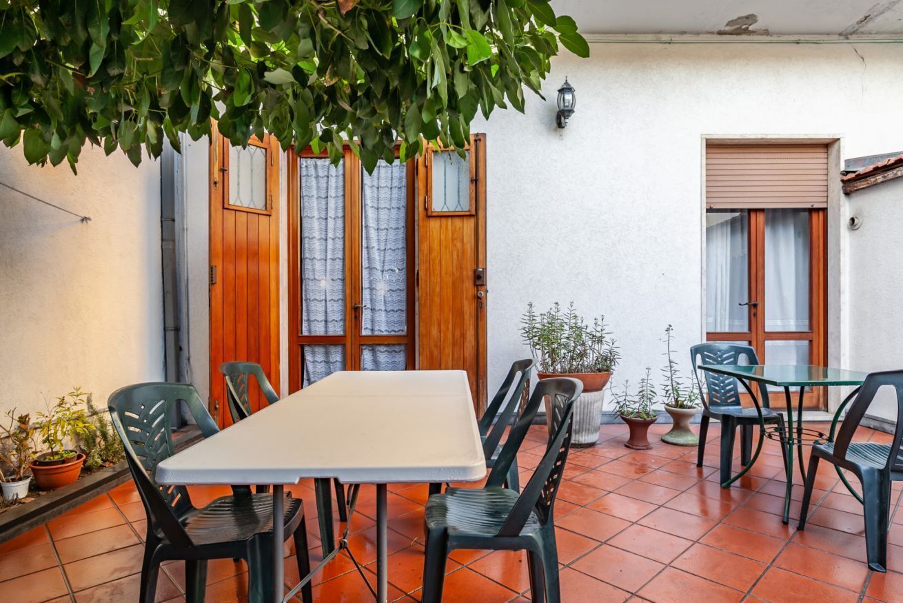 En terrasse med et bord, stole, trædøre og krukker med planter.