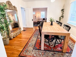 Een eetruimte met een houten tafel en stoelen, een kamerbreed tapijt met dessin en een grote spiegel.