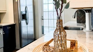 Une cuisine dotée d’un plan de travail en marbre, d’un réfrigérateur en acier inoxydable et d’un vase en osier contenant des feuilles vertes.
