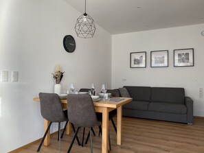 Uma área de refeições moderna com mesa de madeira, cadeiras cinzas e um sofá cinza.