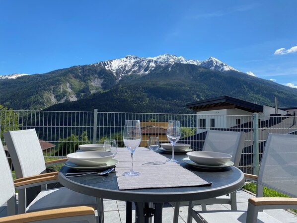 Mesa posta para dois com vista para montanha, cadeiras externas e cerca de metal.