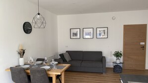 Ett modernt vardagsrum med en matplats, med ett träbord, en grå soffa och en geometrisk hänglampa.