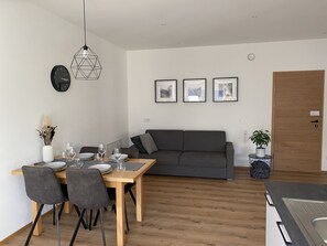 Sala de estar moderna com área de jantar, apresentando uma mesa de madeira, sofá cinza e luminária pendente geométrica.