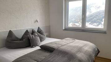 Ein Schlafzimmer mit Bett, grauen Kissen, einer Nachttischlampe und einem Fenster mit Bergblick.