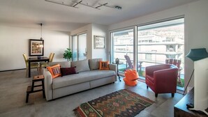 A modern living room with a sofa, chairs, a dining table, and a large window offering a view of buildings.