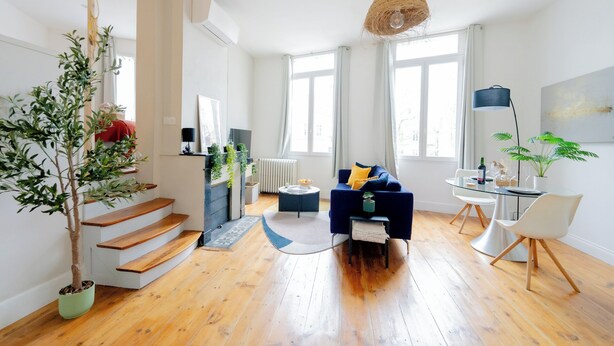 Un salón amplio con escalera, un sofá azul, una mesa de comedor y una lámpara colgante.
