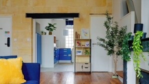 Una sala de estar con un sofá azul, piso de madera, una chimenea y una cocina al fondo.