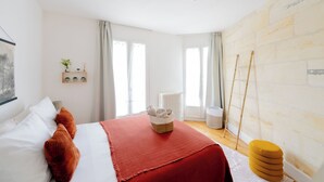 Un dormitorio con una cama, un plaid rojo, una planta pequeña, un radiador y una escalera apoyada en una pared de piedra.