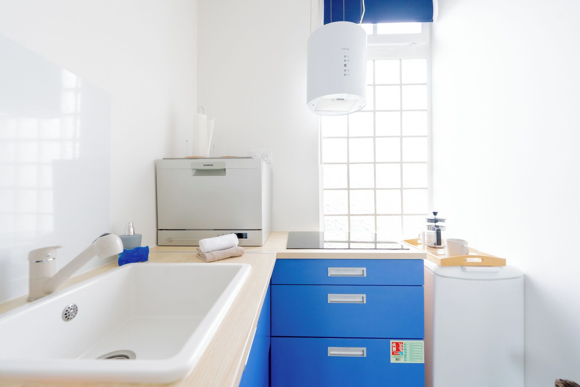 A modern bathroom with a white sink, blue cabinets, a Siemens water heater, and a window with blinds.