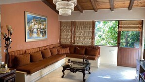 Ein Wohnzimmer mit braunem Sofa, einem Glastisch, einem Stadtbildgemälde und einem großen Fenster mit Jalousien.