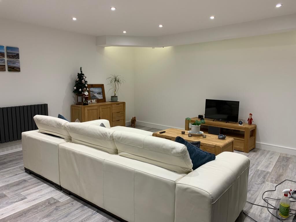 Een moderne woonkamer met een witte bank, een houten salontafel en een tv op een houten dressoir.