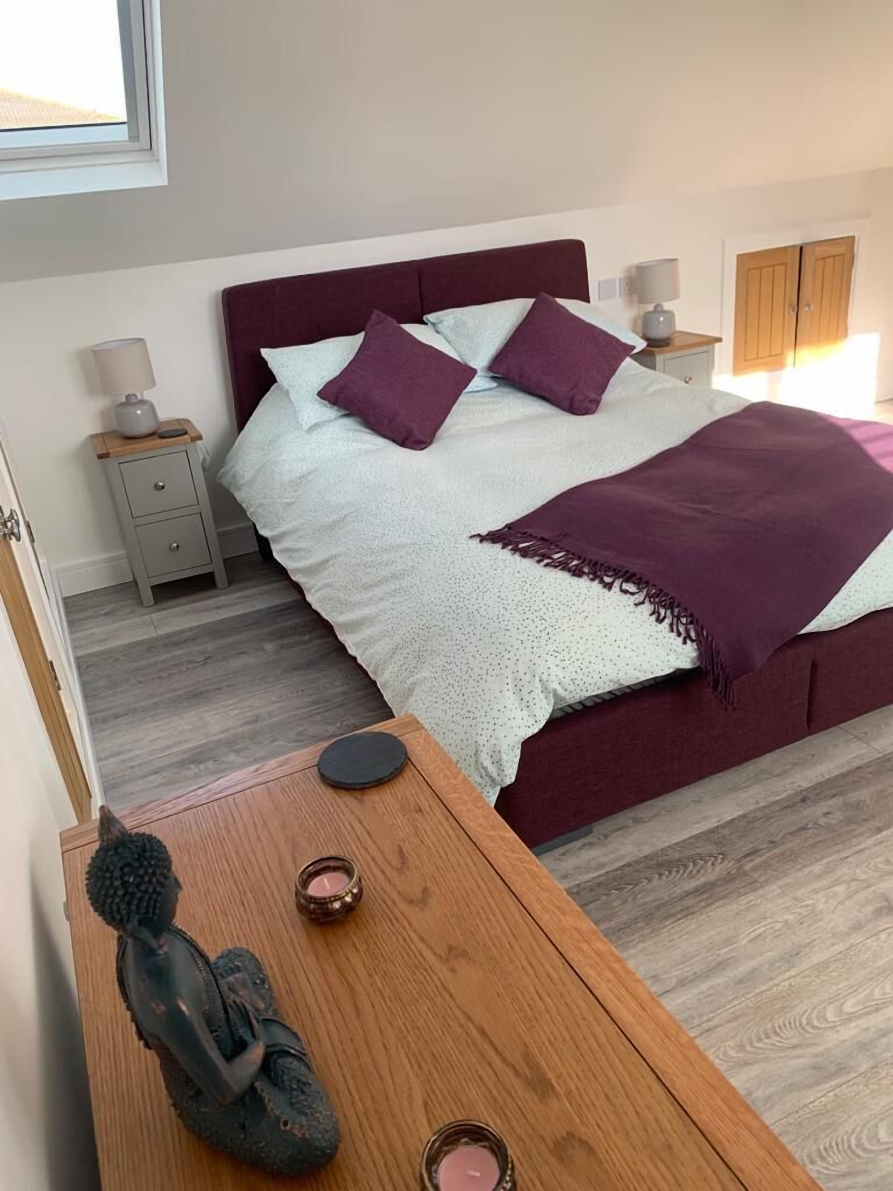 A bedroom with a large bed, two nightstands, a wooden side table, and a statue.