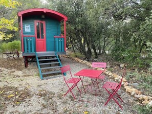 Una cabana petita amb una porta vermella i parets blaves, envoltada d'arbres i un camí de grava.