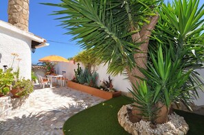 Eine Terrasse mit Steinboden, einem kleinen Tisch mit Stühlen und verschiedenen Topfpflanzen.